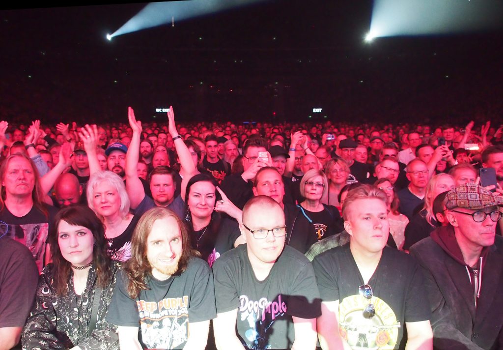 Ihmisiä suuressa areenassa katsomassa rockkonserttia.